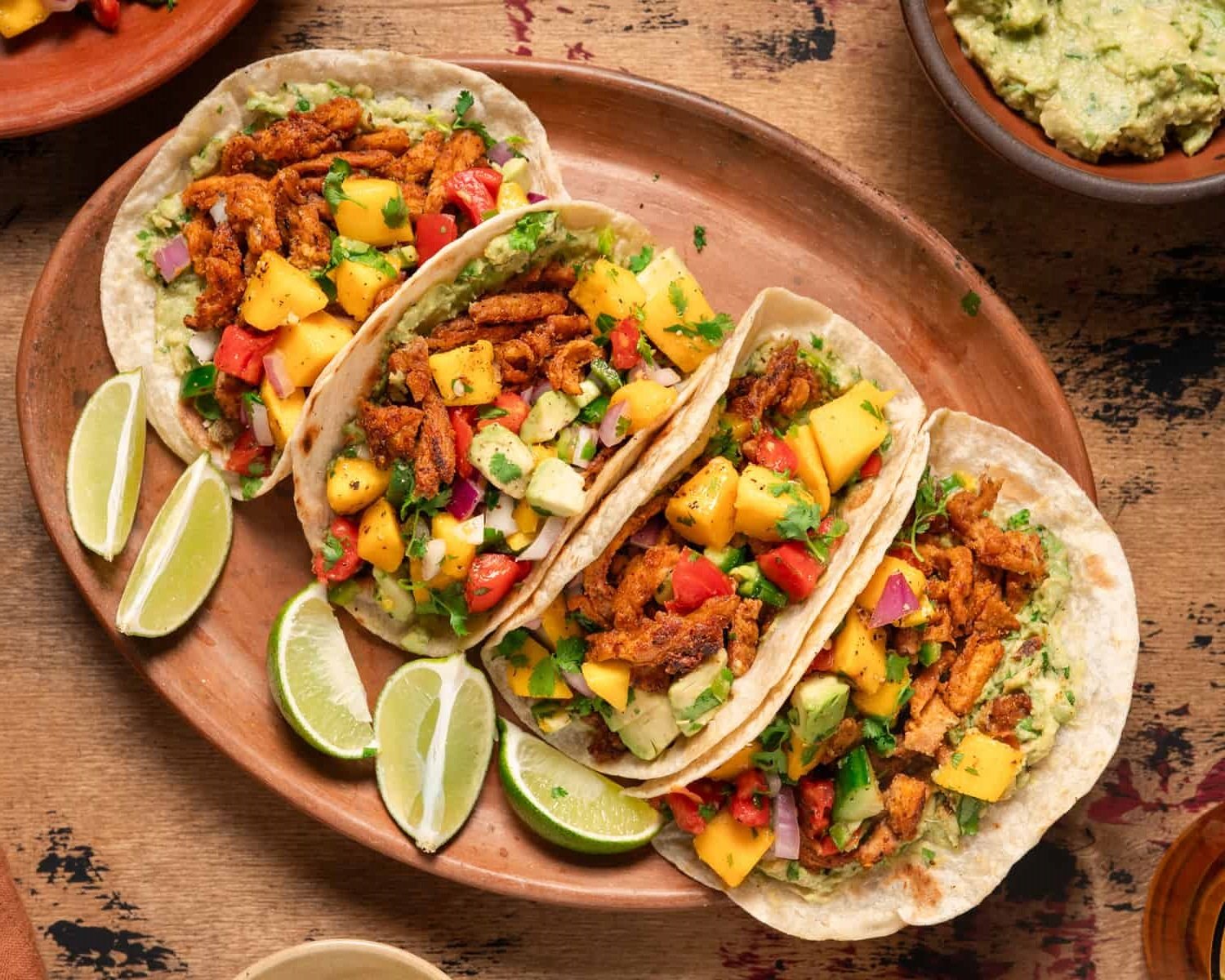 A plate of vegan tacos topped with mango salsa, avocado, and lime wedges